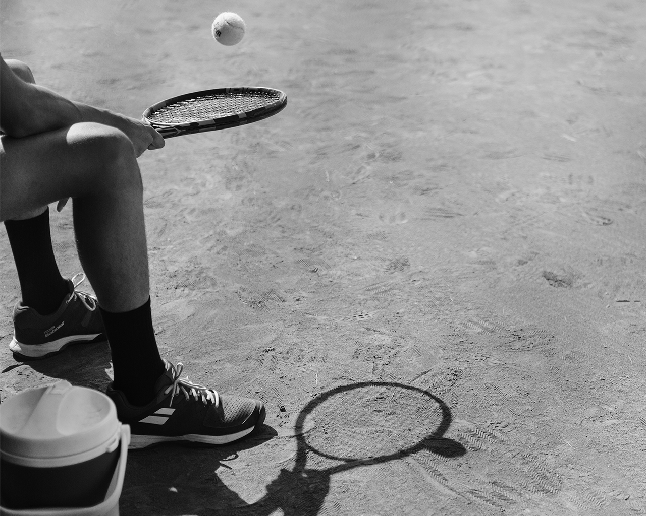 Un tennista assegut amb la seva raqueta i una pilota en l'aire en una pista de terra batuda, durant un programa d'impuls al talent de la Fundació Ferrer.