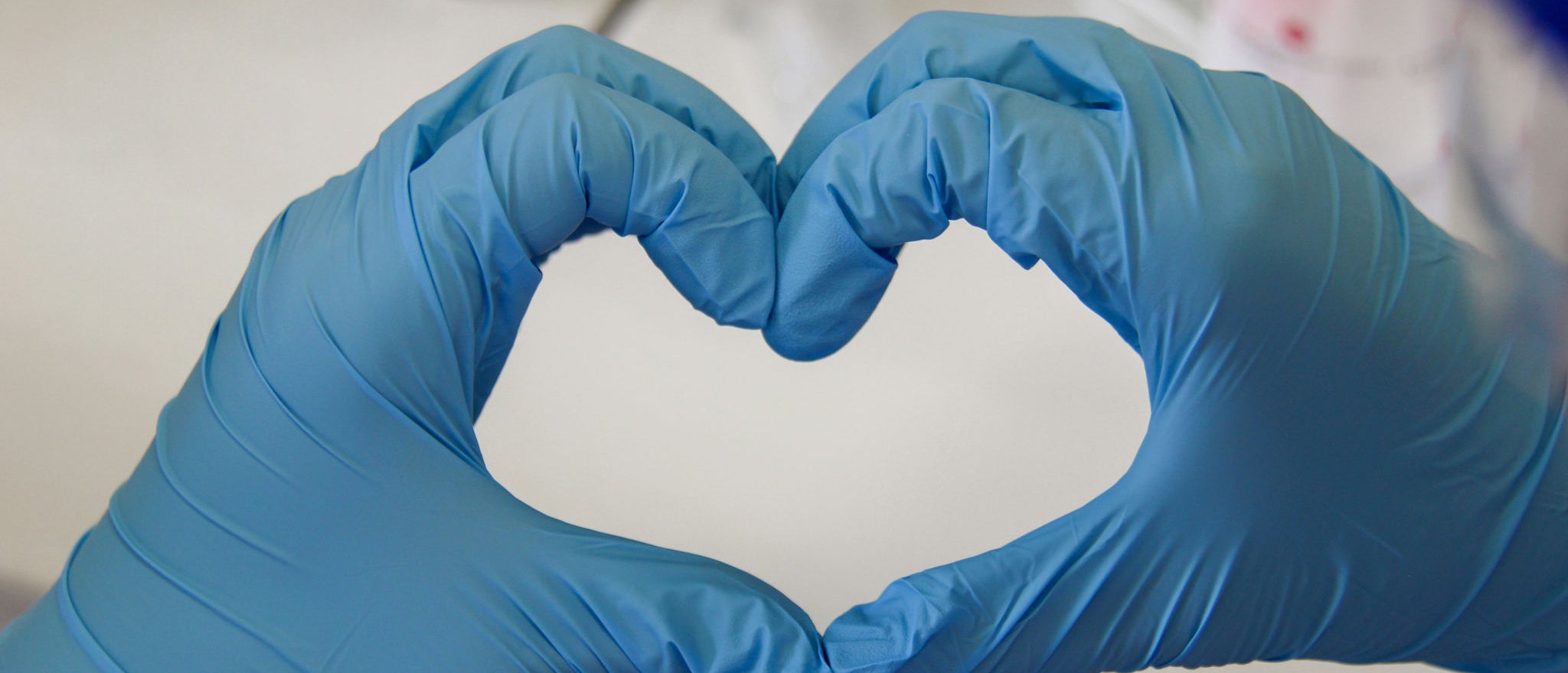 Hands with blue gloves form a heart in a laboratory environment, representing Ferrer's commitment to care, science and health.