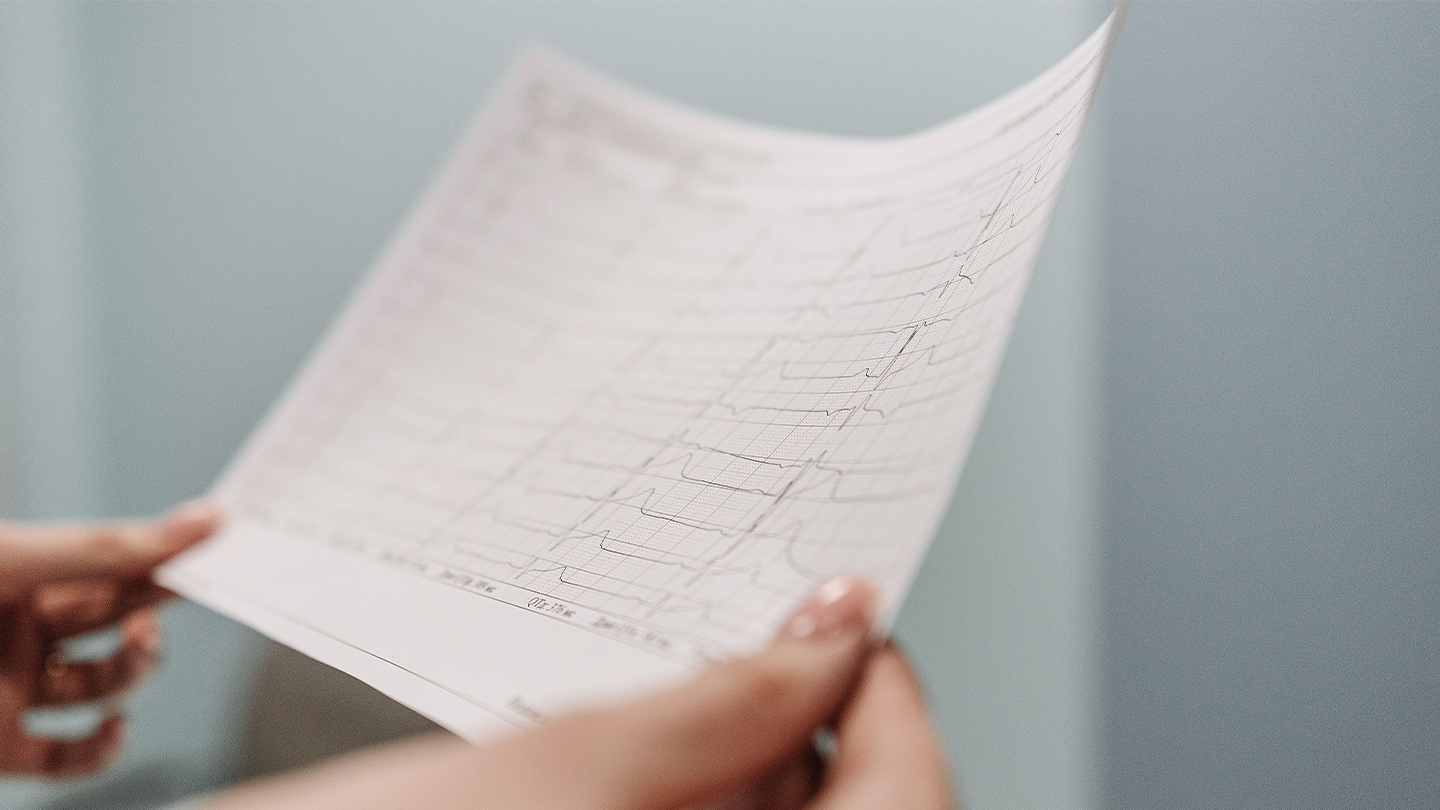 One pair of hands holds and closely examines a piece of paper with the results of an electrocardiogram printed out.