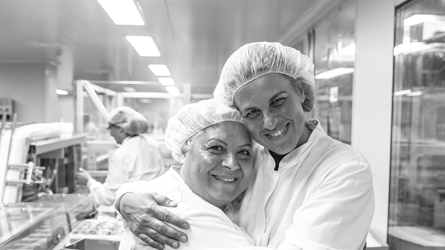 Two laboratory operators from the Ferrer company smiling as they hug each other on the production floor.