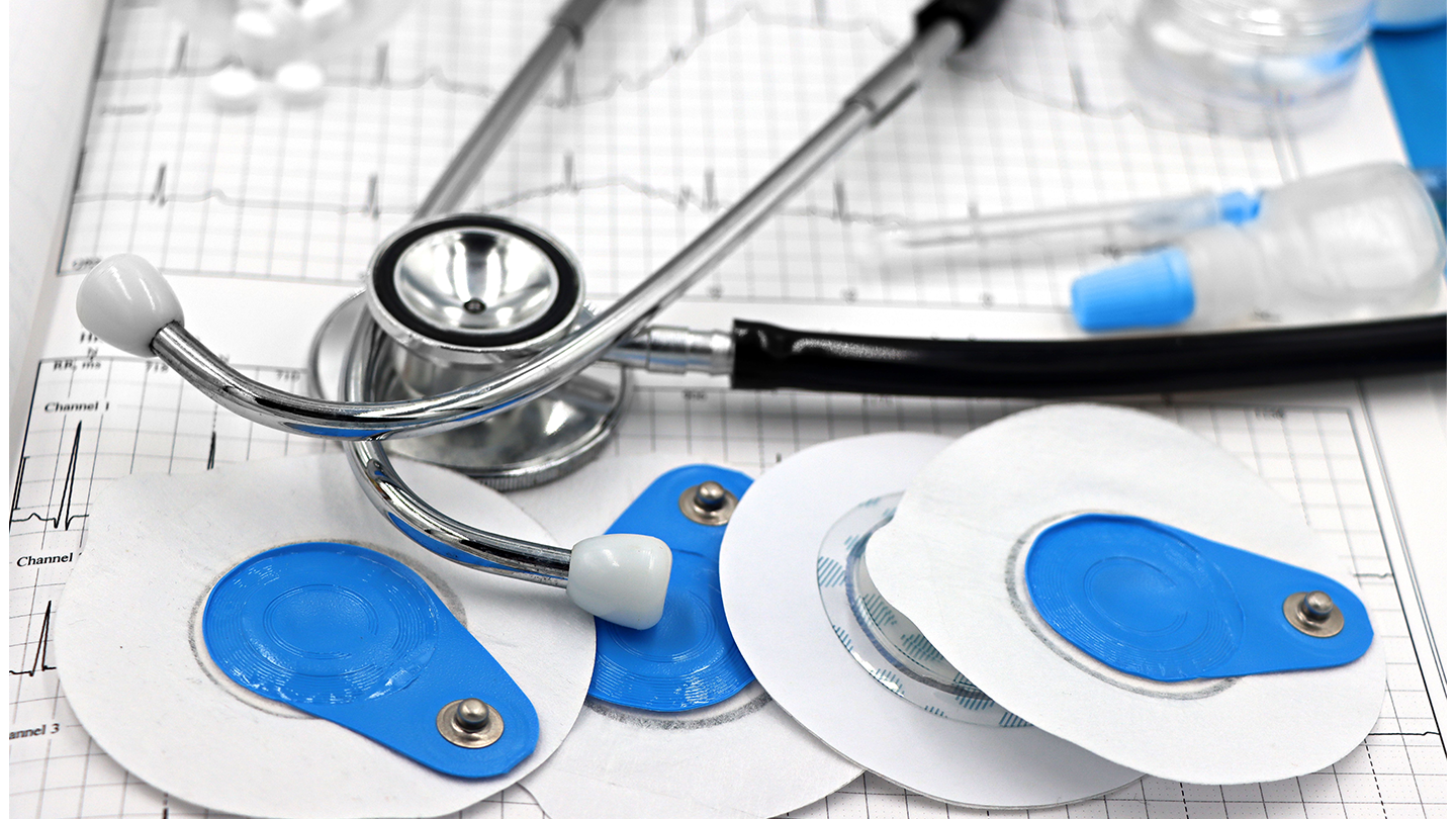Un estetoscopi i diversos elèctrodes d' electrocardiograma de color blau i blanc reposen sobre un informe mèdic imprès.