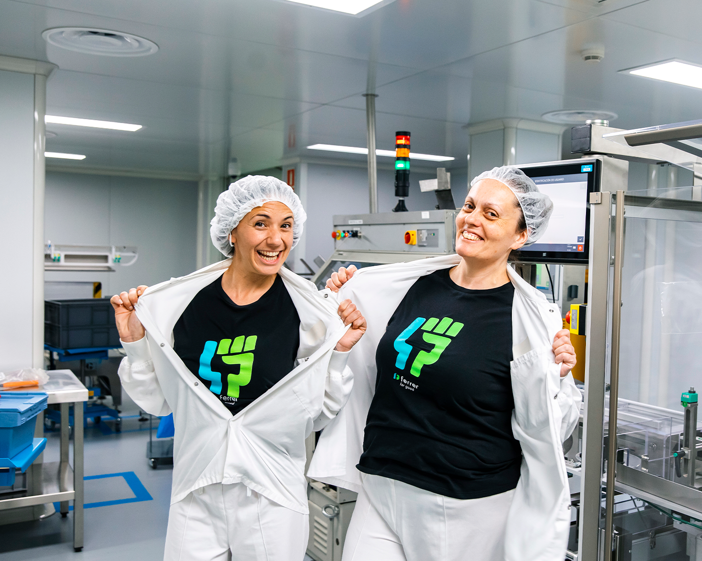 Dues operàries de Grup Ferrer mostrant orgulloses el seu compromís amb l'equip Great People a la planta farmacèutica.