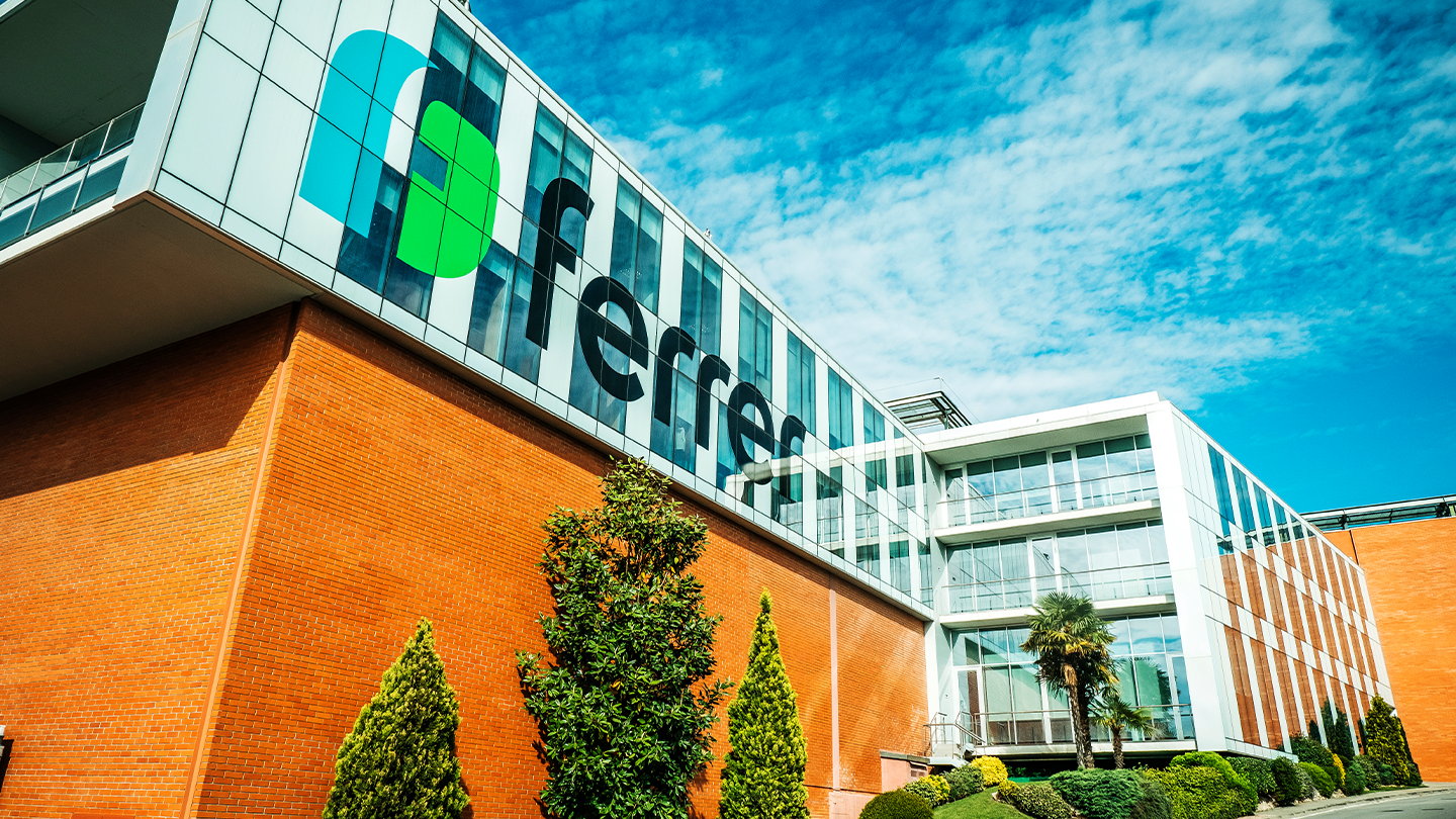 Angled view of the exterior of a modern corporate building with the Ferrer logo and inscription on the façade under a blue sky with clouds.