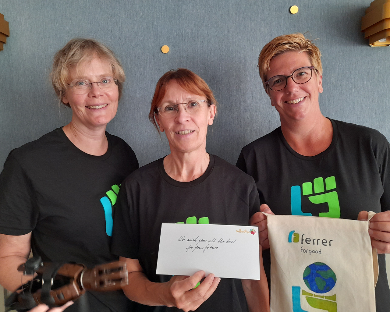 Three people from the Ferrer team smile at the camera showing corporate materials of the company, in a close and collaborative atmosphere.