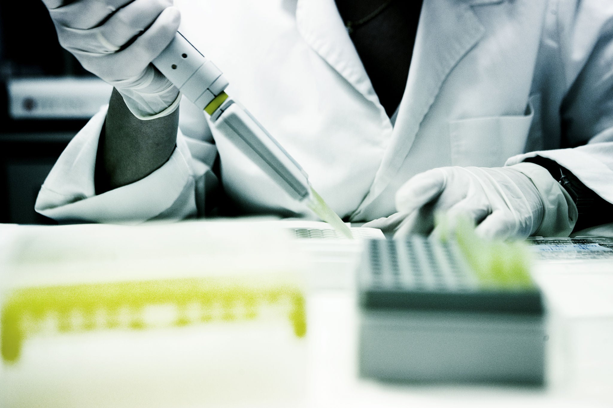 A person in a laboratory using an automatic pipette to handle samples, wearing a white coat and protective gloves.