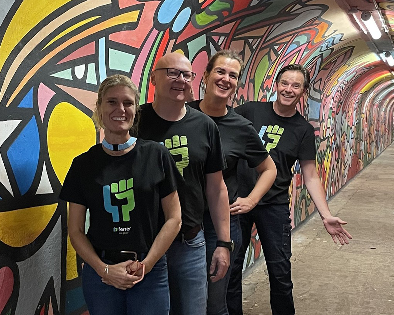 Ferrer team smiling in a tunnel with street art, wearing company corporate t-shirts.