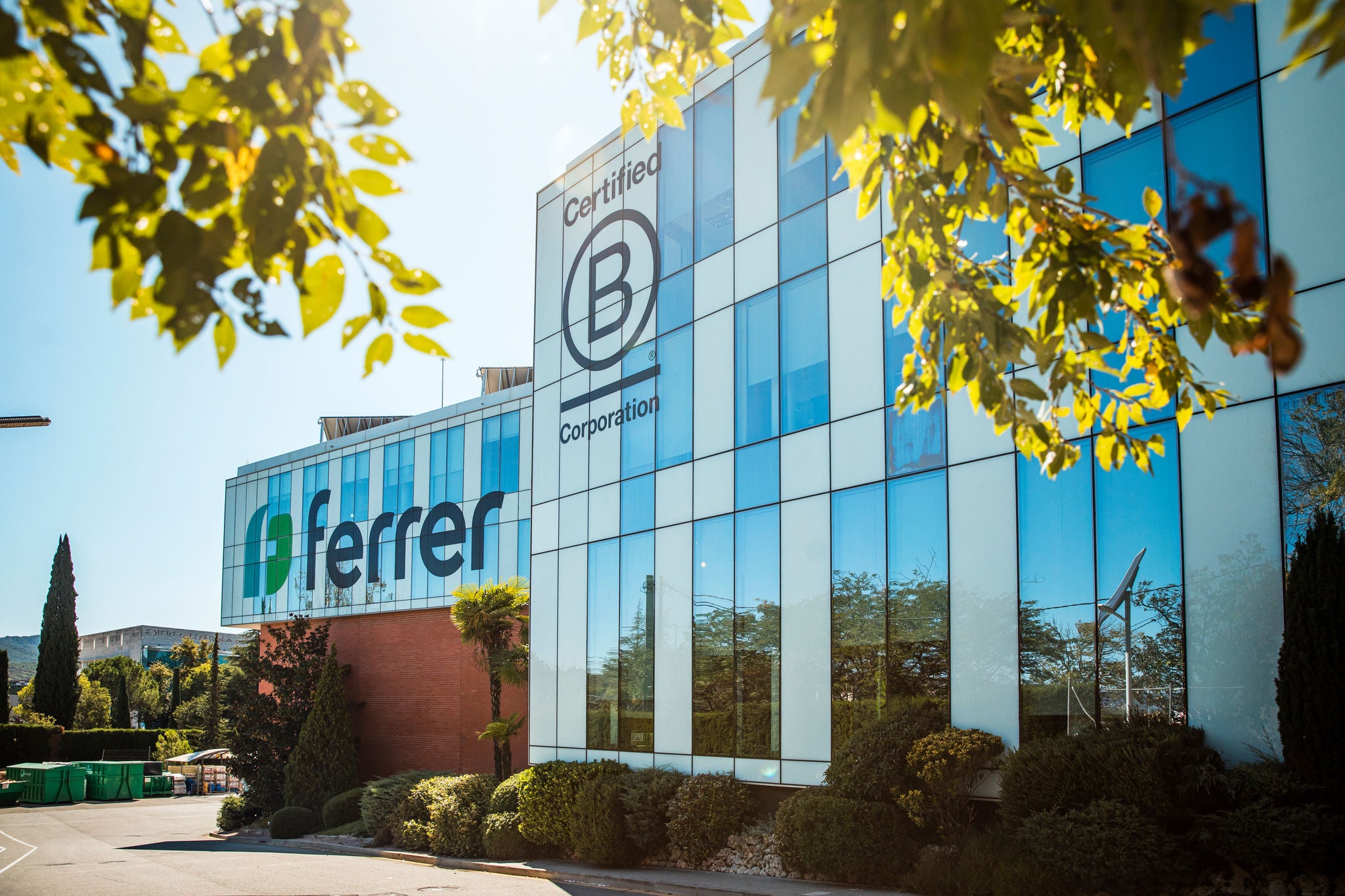 Façade of the Ferrer Laboratories building with blue glass, shrubs at the base and the Certified B Corporation logo in the foreground.
