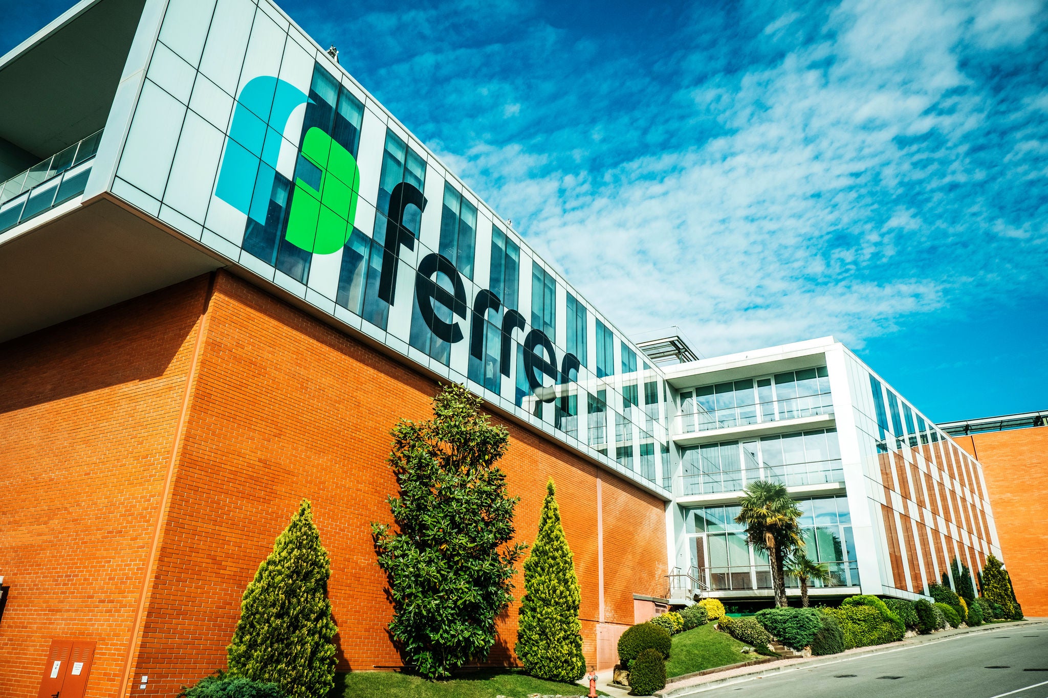 Ferrer corporate building with large logo on the glass façade, brick cladding and manicured gardens under a blue sky.
