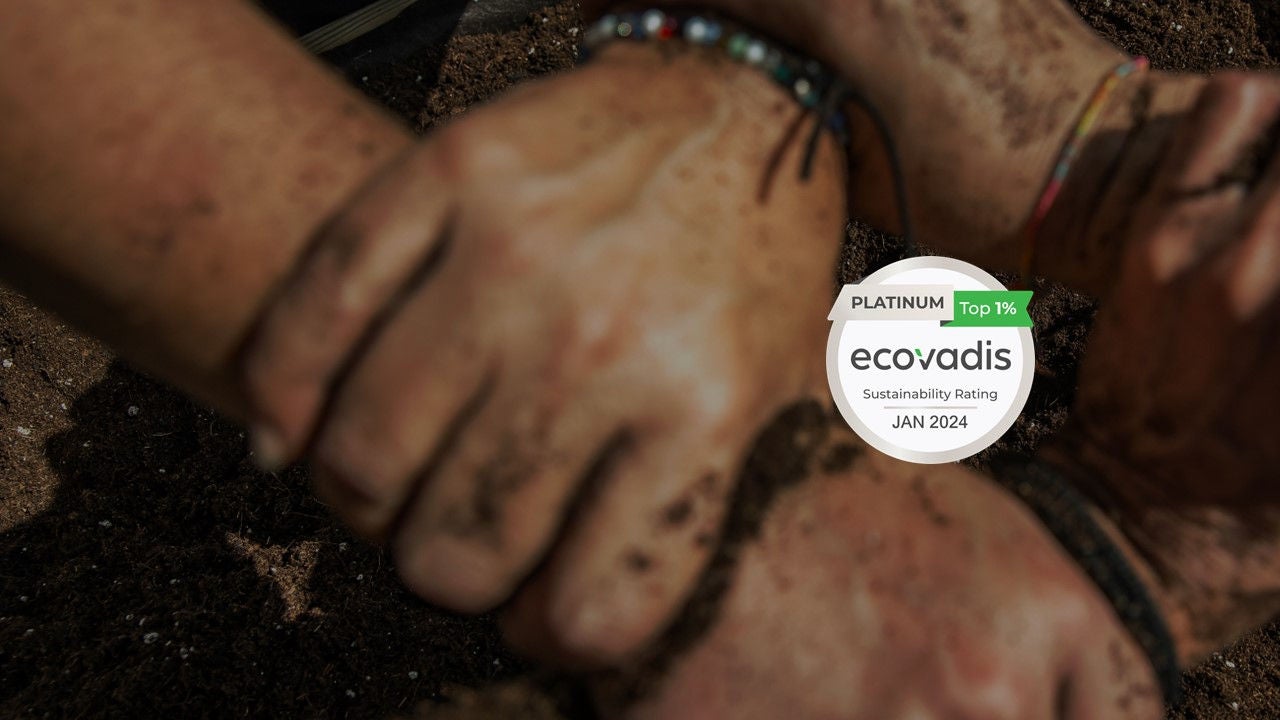 Primer pla de diverses mans unides i tacades de terra, al costat d'un segell d'EcoVadis que reconeix Ferrer amb la qualificació Platinum Top 1% en sostenibilitat.