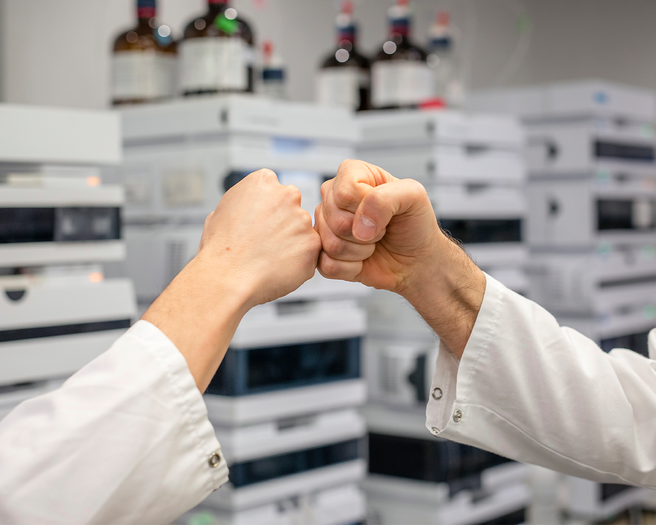 Scientists fist bumping in a research laboratory, symbolizing the success of a collaboration agreement with Ferrer's business development department.