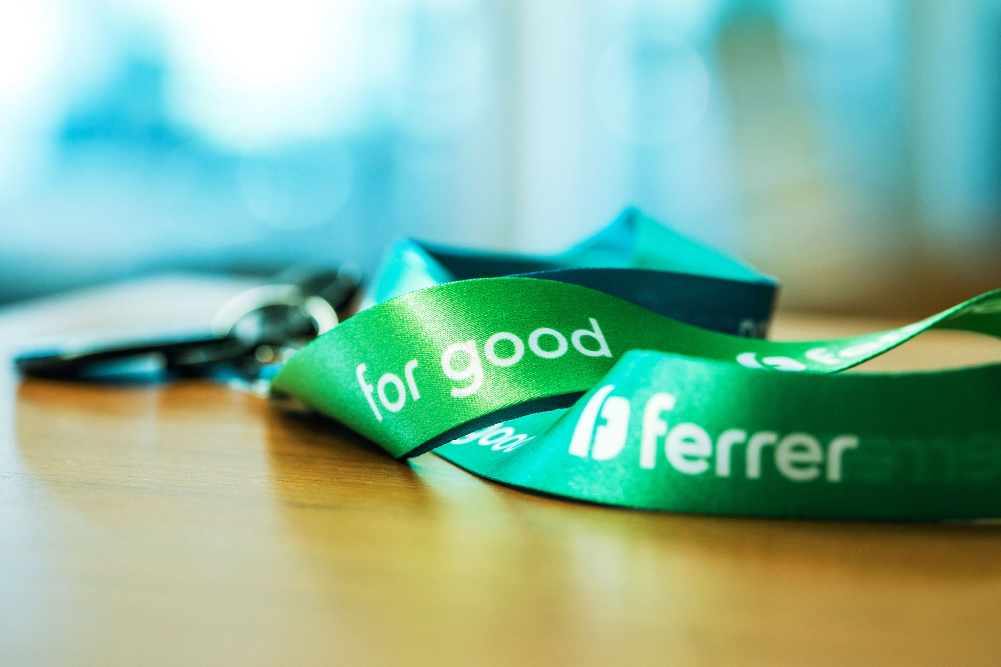 Cinta verda corporativa de Ferrer sobre una taula de fusta, amb el lema "for good" en primer pla i el fons desenfocat.