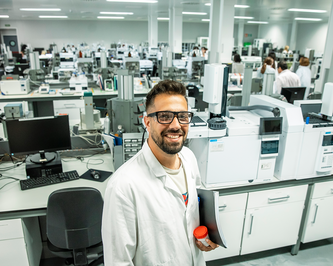 Profesional de Ferrer sonriendo a cámara en un laboratorio, rodeado de equipos de análisis y tecnología científica.