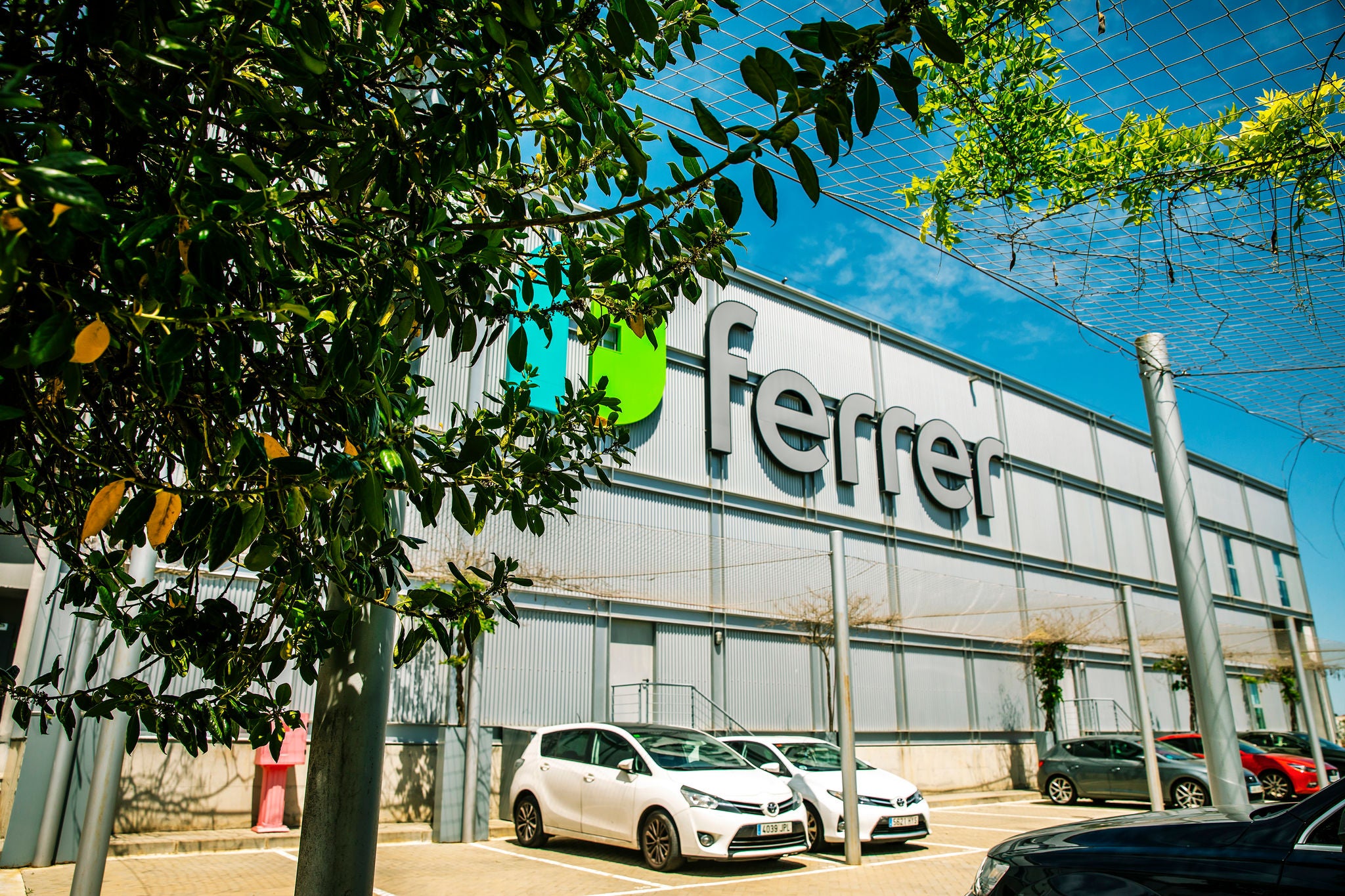 Fachada del centro logístico de Ferrer con el logotipo de la compañía, vehículos estacionados y zonas verdes alrededor.