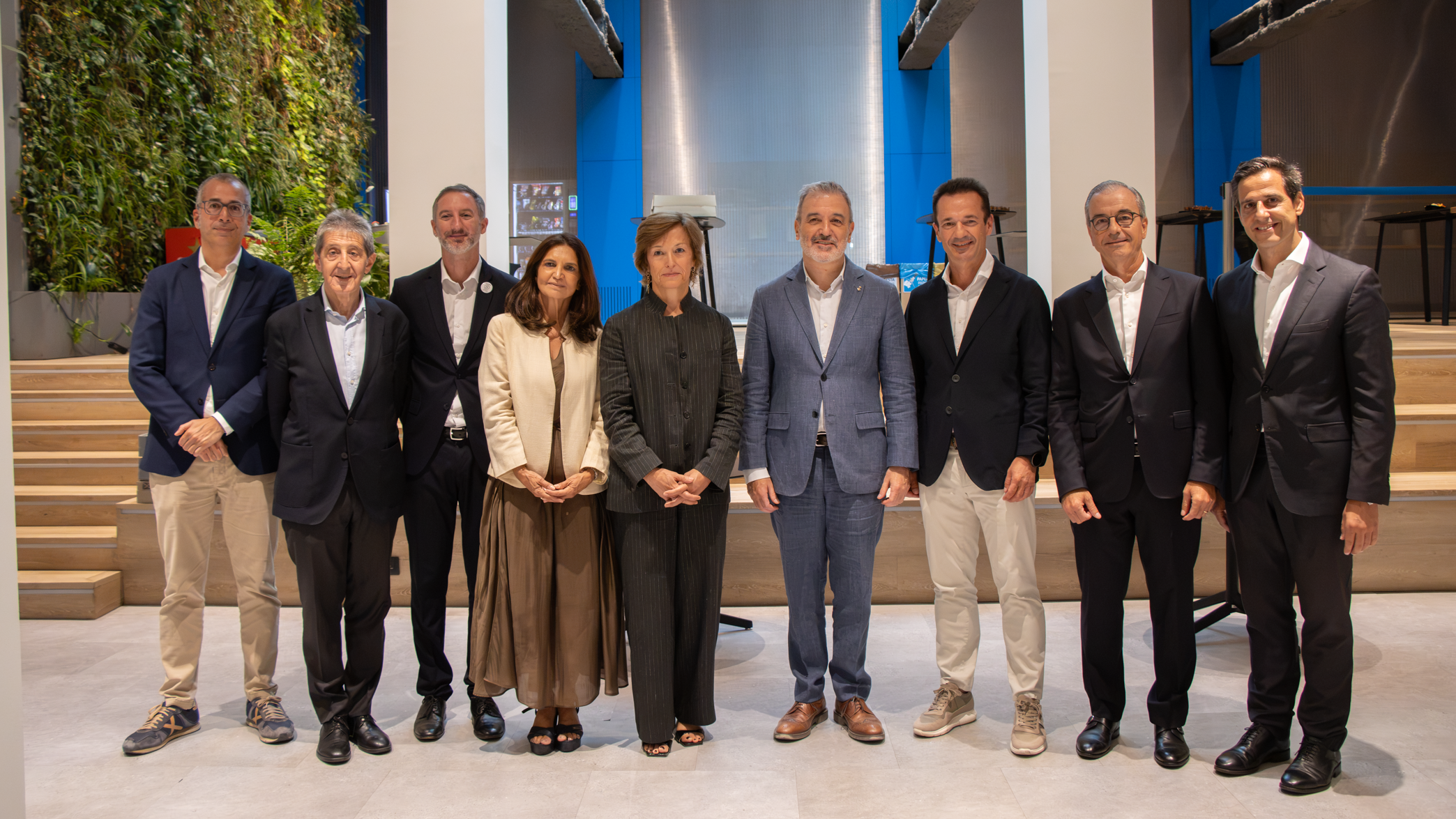 Grupo de ocho profesionales posando alineados en un espacio moderno de techos altos con un jardín vertical al fondo.