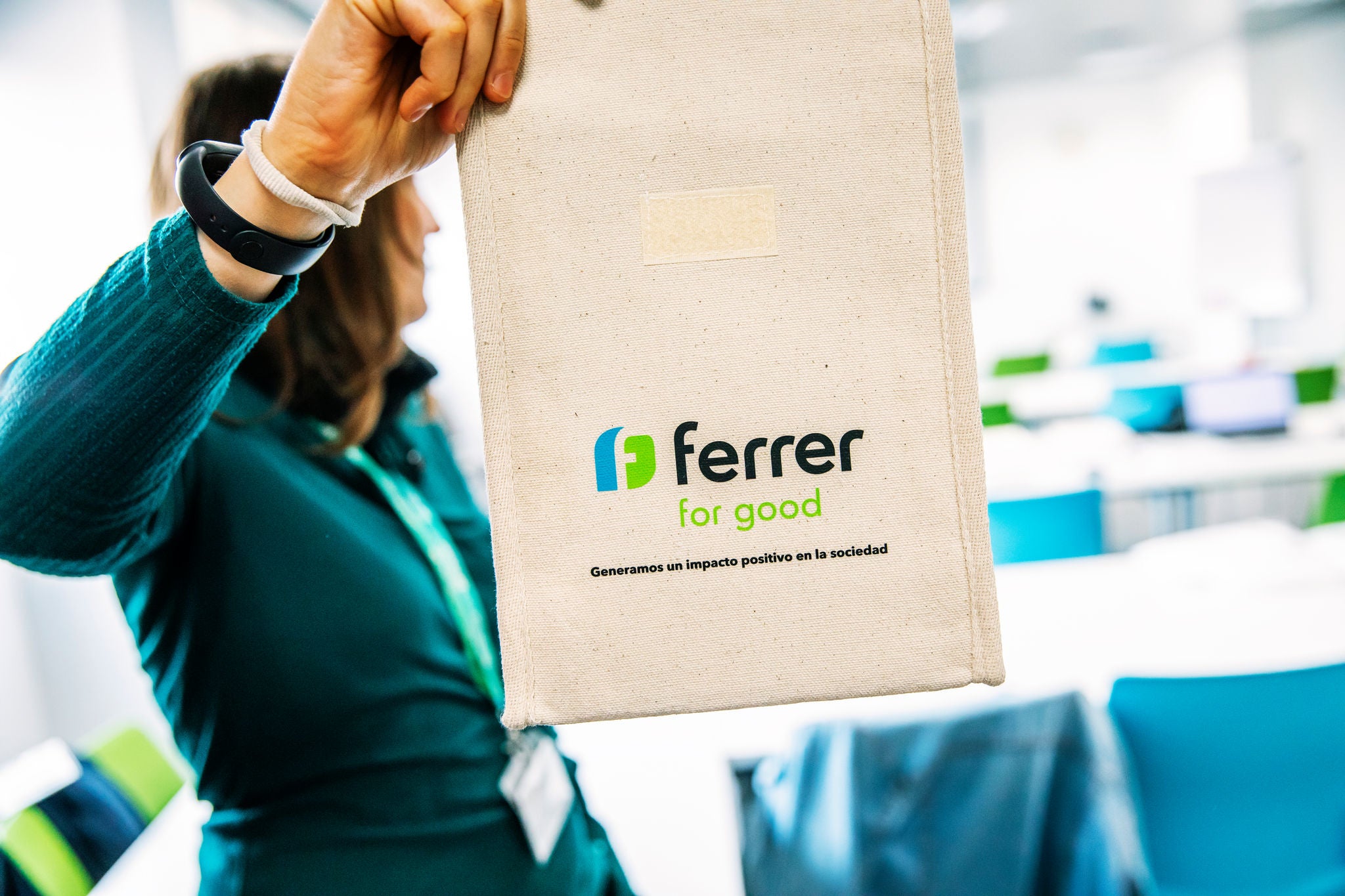 Persona sosté una bossa reutilitzable de tela amb el logo "Ferrer for Good" en un espai interior lluminós, relacionat amb una activitat corporativa o de voluntariat de Ferrer.