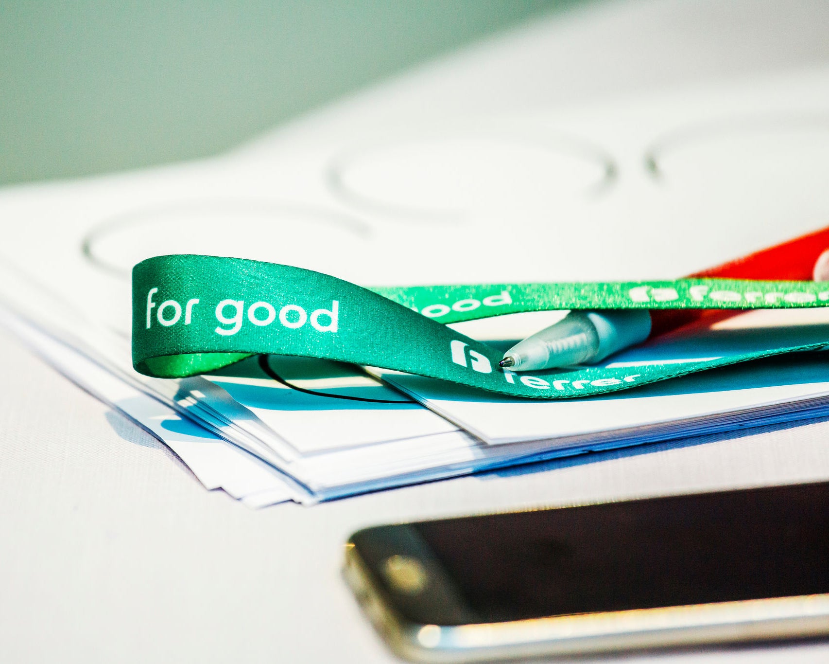 Detalle de una mesa de trabajo con documentos, un móvil y una cinta verde de Ferrer con el mensaje “Ferrer for good”.