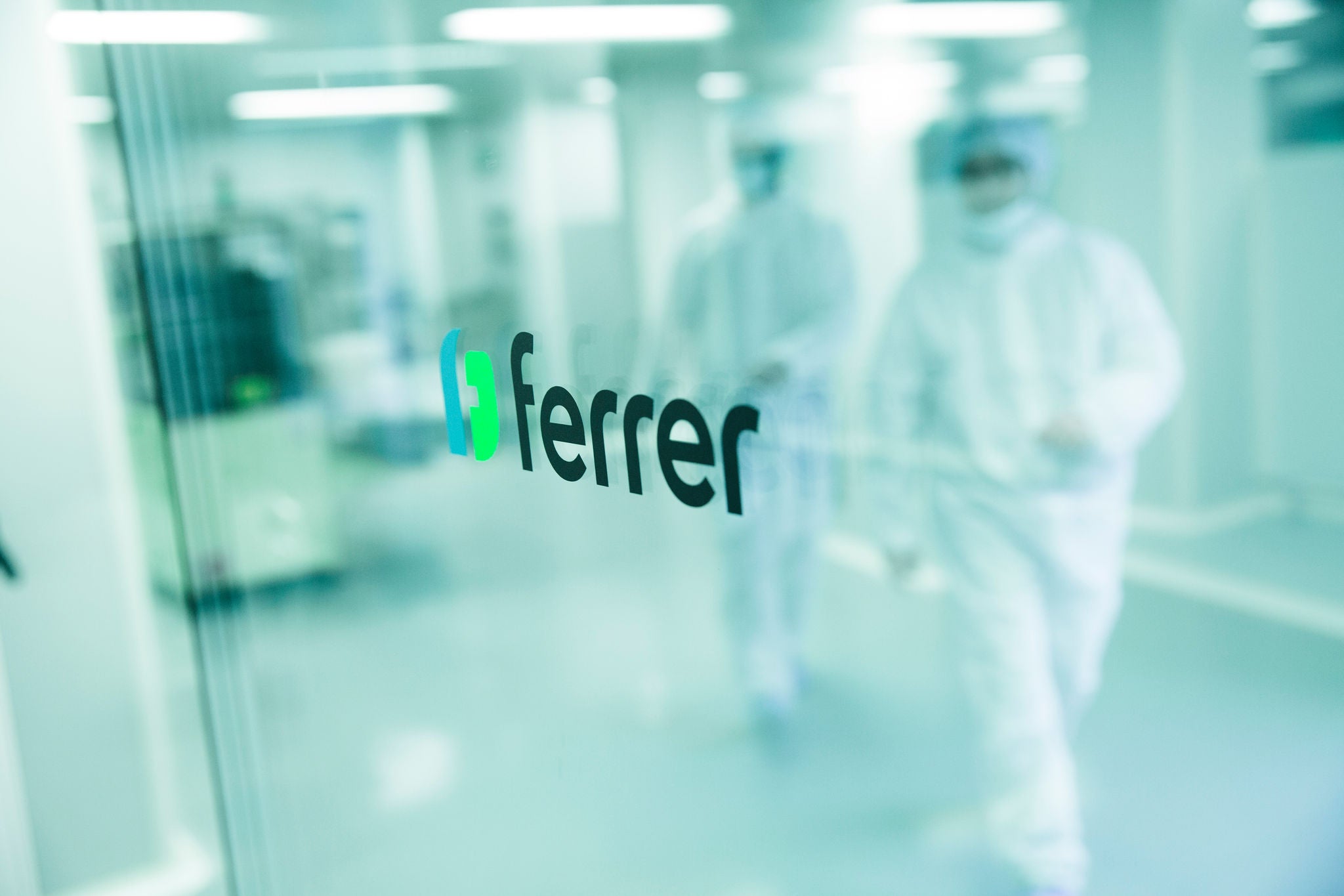 Ferrer logo on a glass door, with two professionals in the background out of focus in a laboratory or production environment.