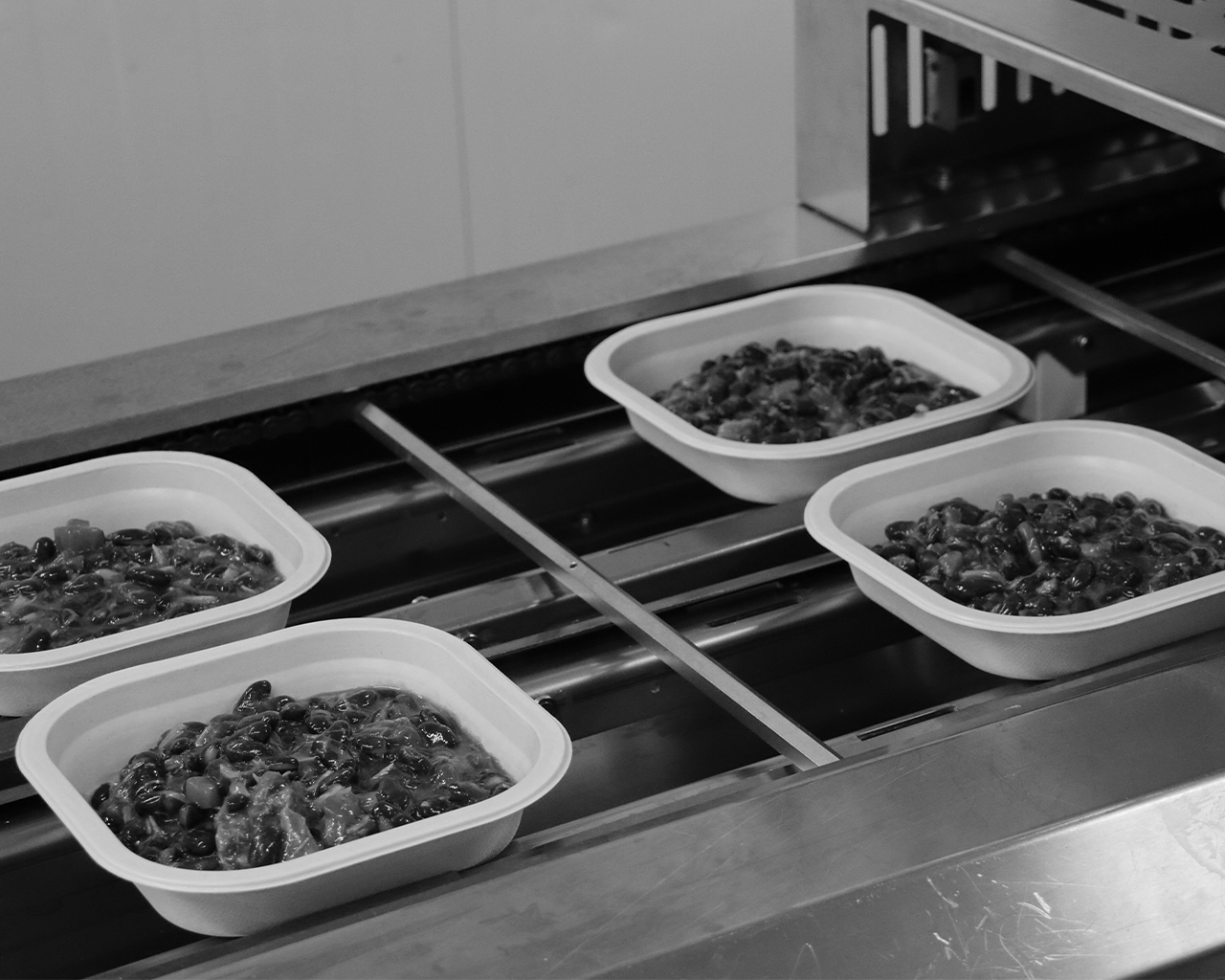 Bandejas con raciones de comida preparada en una cinta transportadora durante un proyecto de cocina solidaria apoyado por el grupo Ferrer.