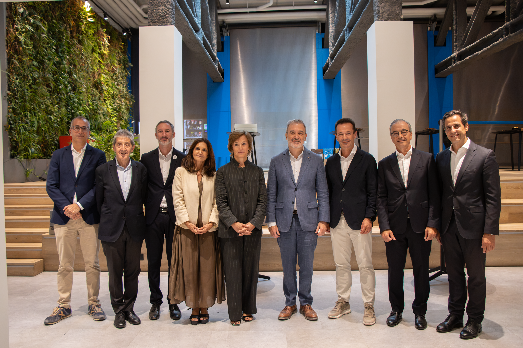 Grup de vuit professionals posant alineats en un espai modern de sostres alts amb un jardí vertical al fons.
