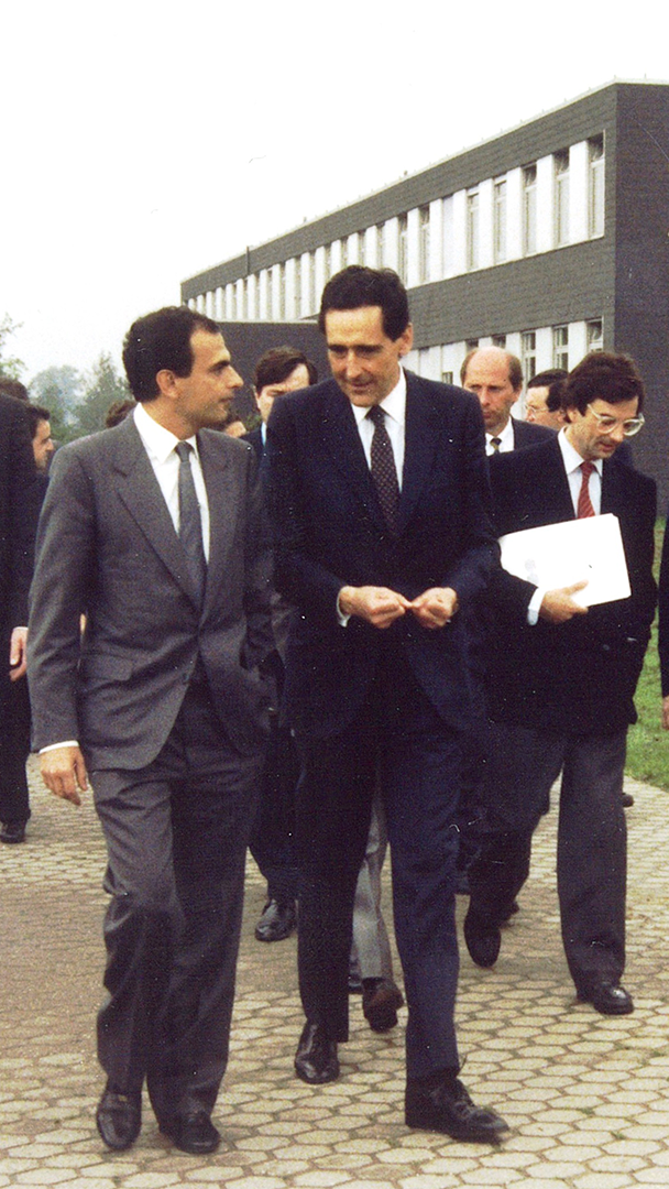 Fotografia d' arxiu d' un grup d' homes amb vestits formals caminant i conversant a l' exterior d' un edifici d' oficines.