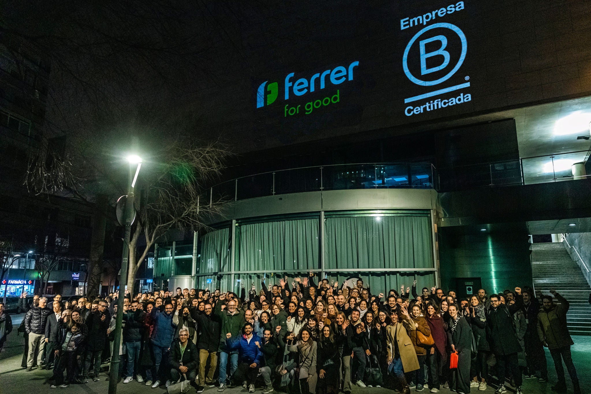 A large group of people posing at night outside a glass building, in an image of a corporate and celebratory atmosphere.