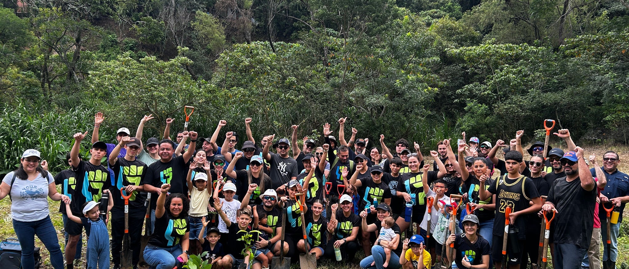 Voluntaris de Ferrer posen en grup en una zona verda i boscosa, amb pales i plantes, celebrant una jornada de reforestació o voluntariat ambiental.
