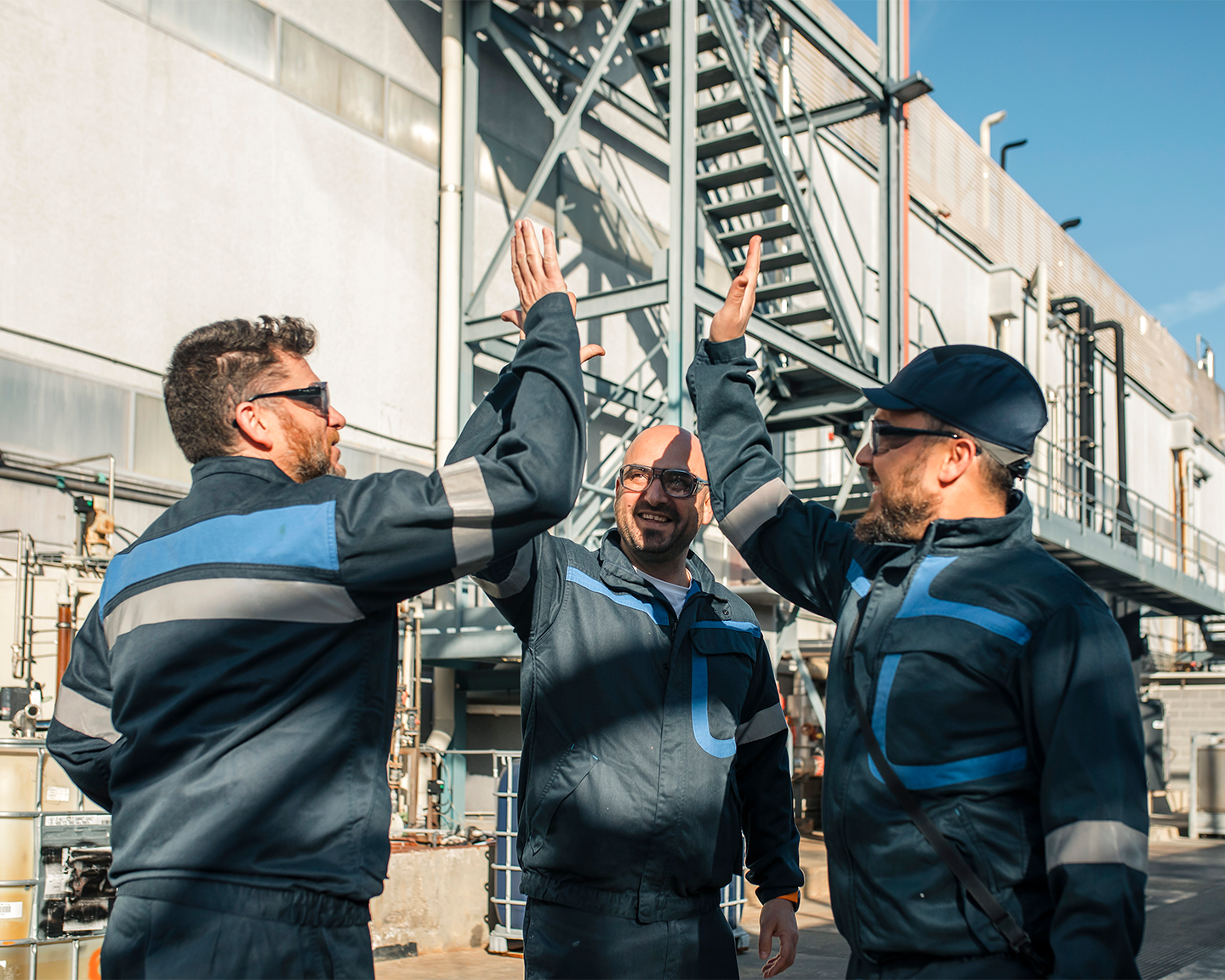 Tres operaris xocant les mans en equip davant les instal·lacions de la fàbrica industrial del Grup Ferrer.