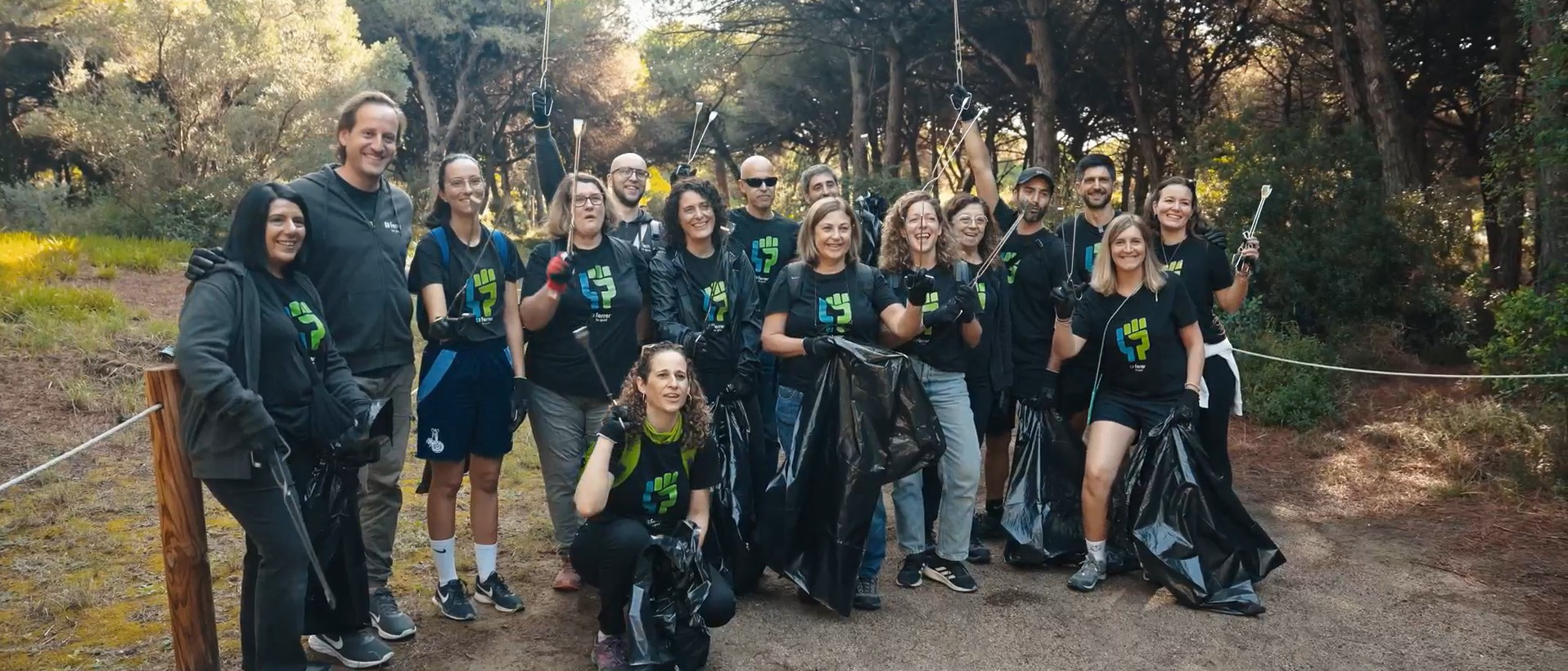 Grup de voluntàries de Ferrer en un entorn natural, somriure a càmera durant una activitat de neteja i recollida de residus, amb bosses i guants.