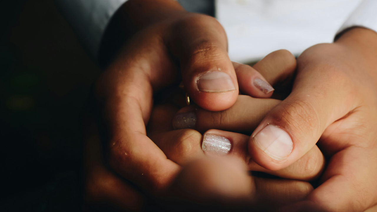 Close-up of joined hands holding each other tightly in a gesture of support, comfort or complicity.
