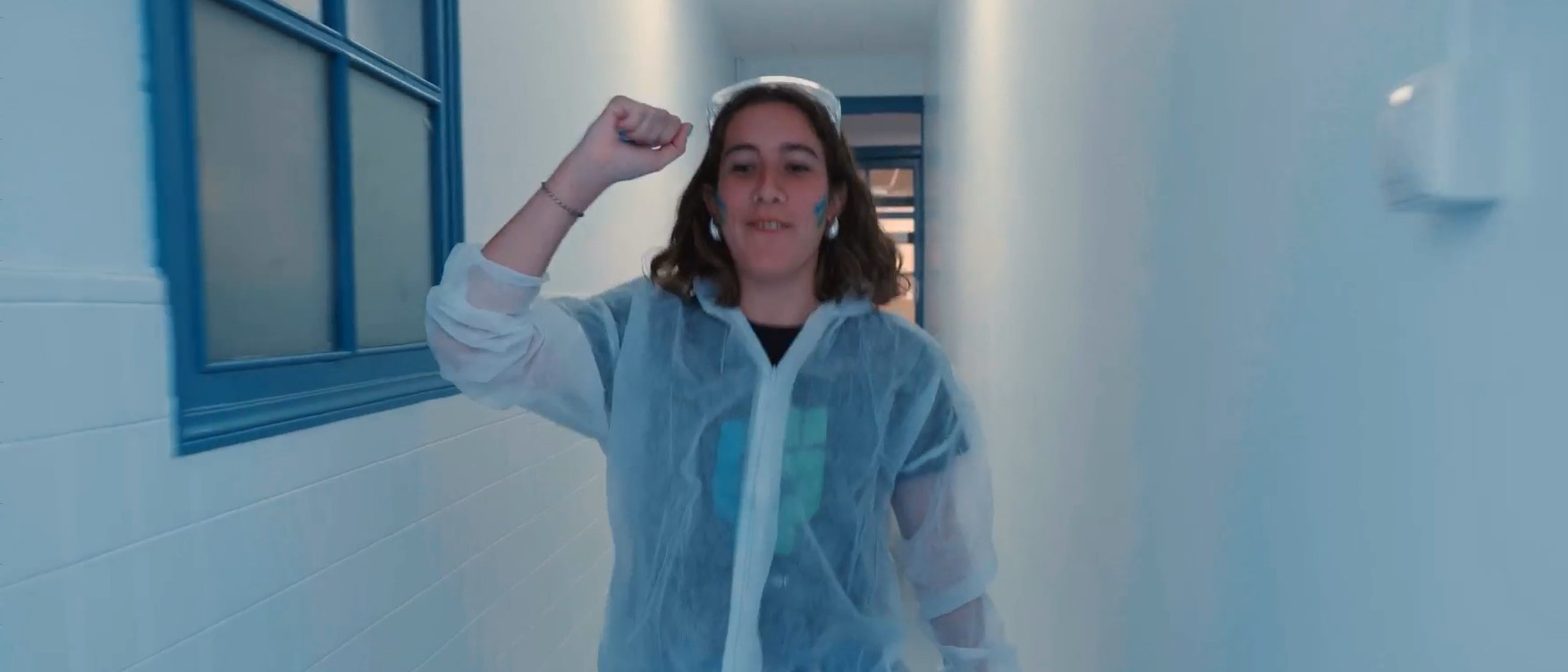 Ferrer professional in a laboratory or production plant environment, dressed in a gown and protective gear, raising her arm in energy or commitment.