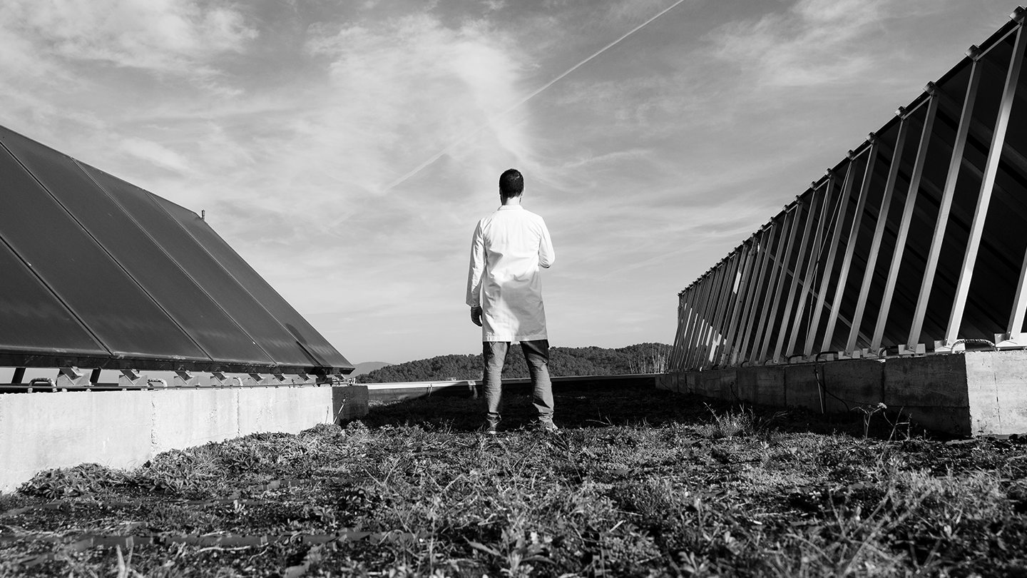 Un profesional con bata blanca observando una instalación de paneles solares sobre un suelo vegetal en la empresa Ferrer.