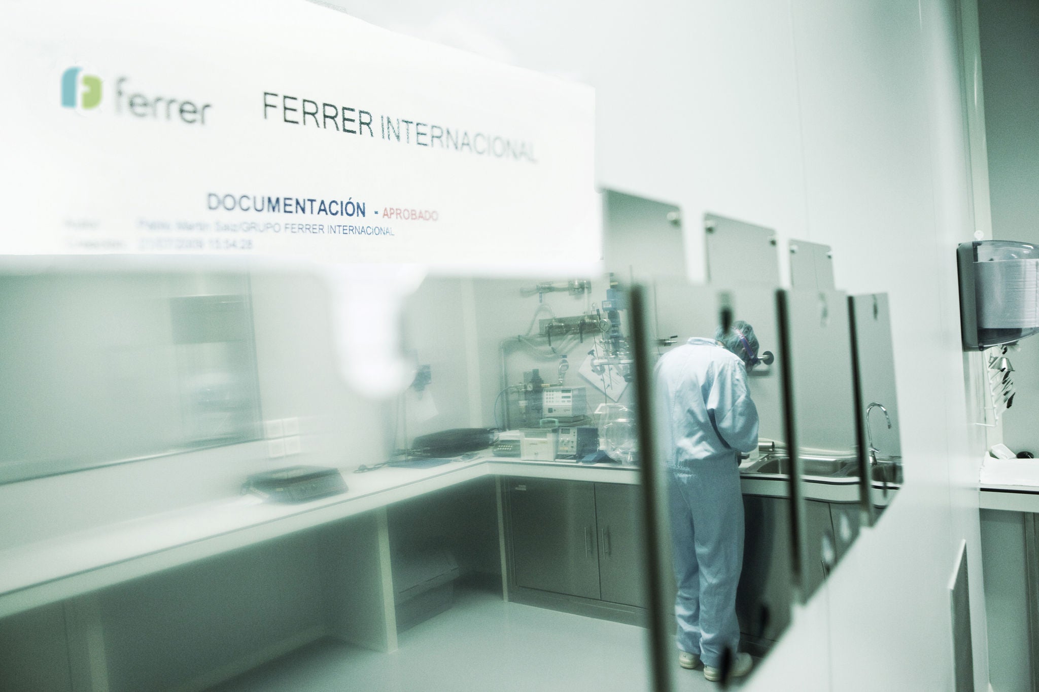 Vista d'una àrea de documentació en instal·lacions de Ferrer Internacional, amb una persona treballant en un entorn tècnic o de laboratori després d'una zona envidrada.