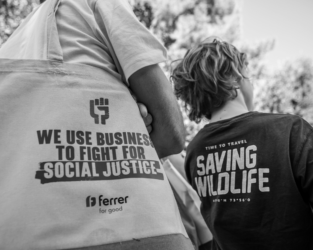 Close-up of an eco-friendly cloth bag from the company Ferrer for good next to a person wearing a biodiversity protection T-shirt at an environmental event.
