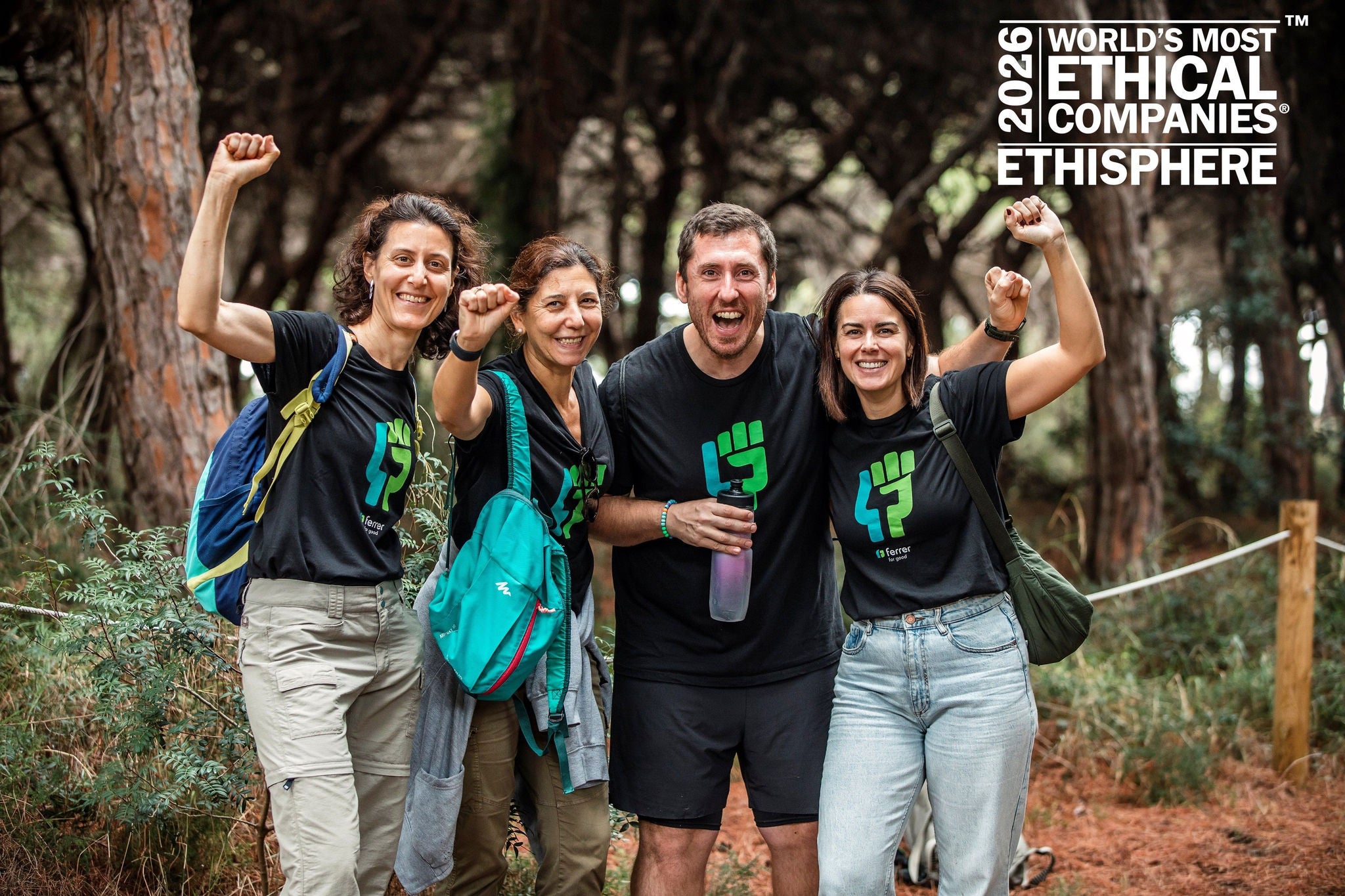 Cuatro personas sonrientes con camisetas a juego celebrando en un bosque con los puños en alto.
