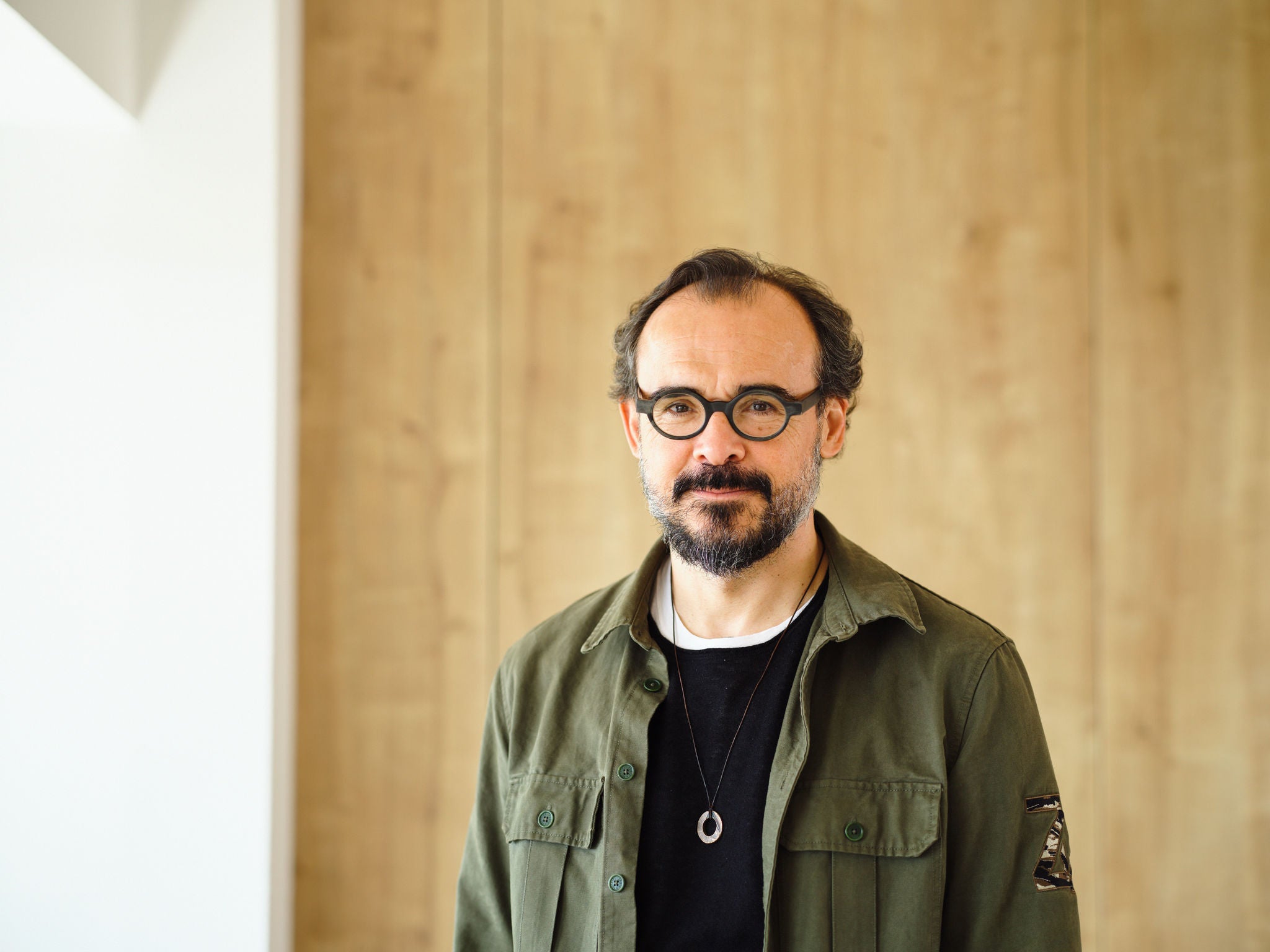 Retrat de Sergi Ferrer-Salat, amb ulleres, barba i camisa verda, posant davant una paret de fusta clara.