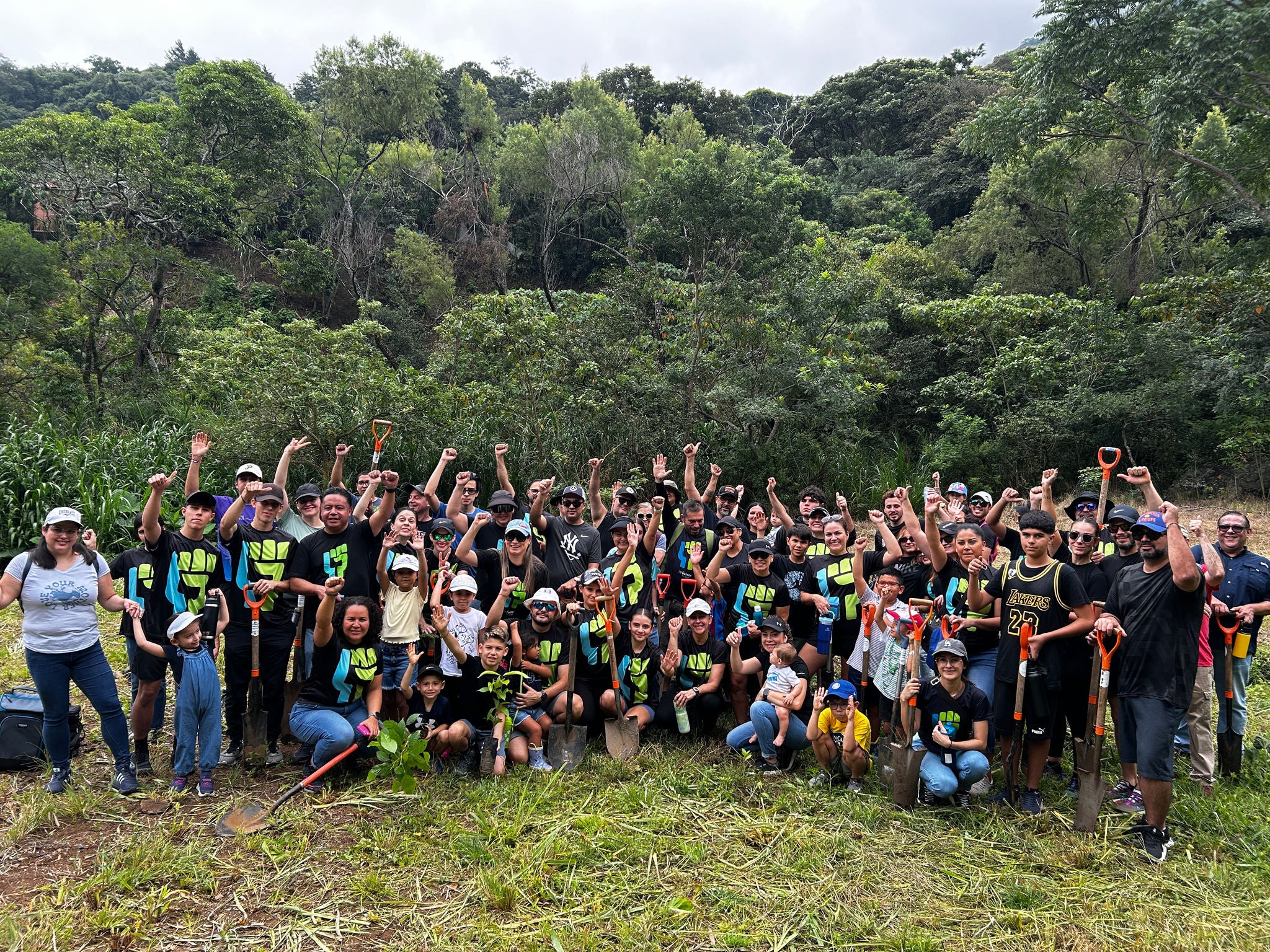 Ferrer volunteers pose in a group in a green and wooded area, with shovels and plants, celebrating a day of reforestation or environmental volunteering.