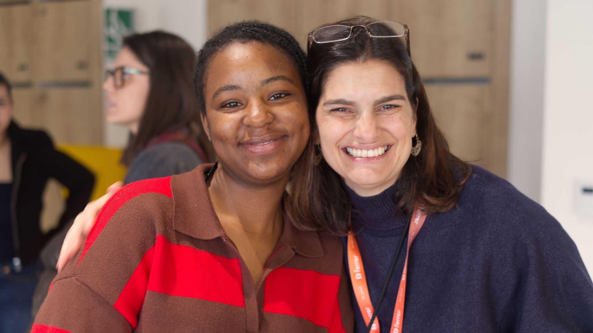 Two smiling women pose embracing in an indoor space.