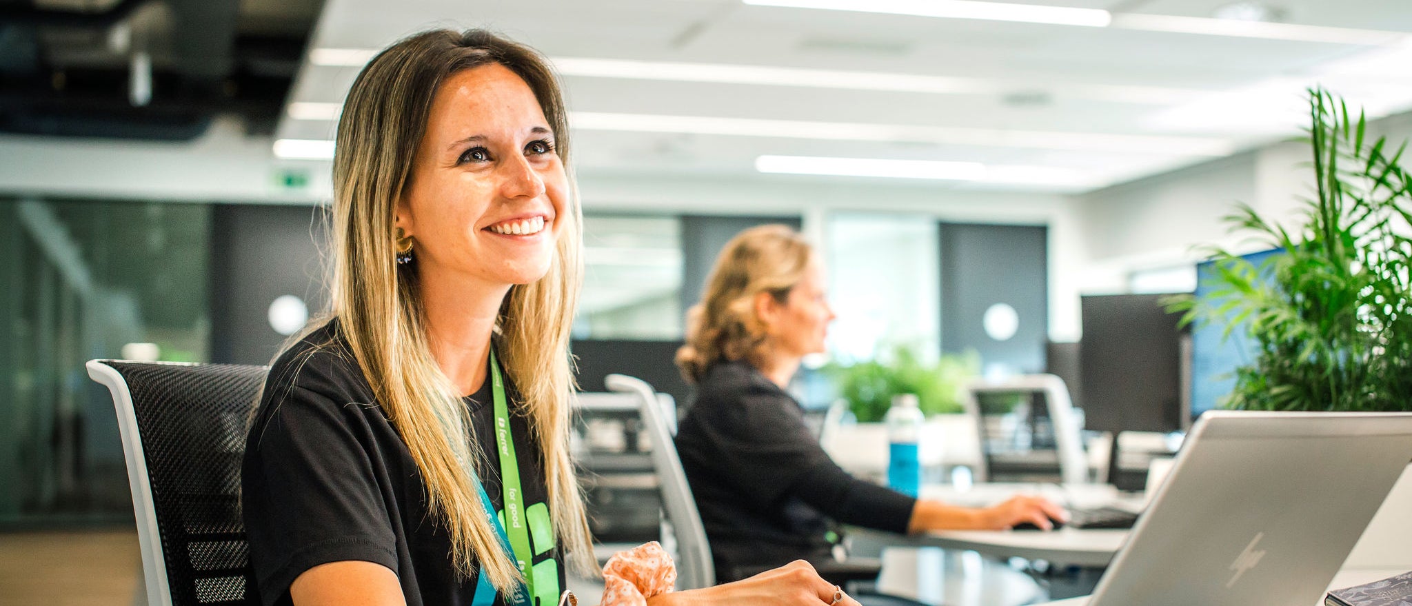 Ferrer's employee smiles as she works with a laptop in a modern, bright office, with another person in the background and a collaborative environment.