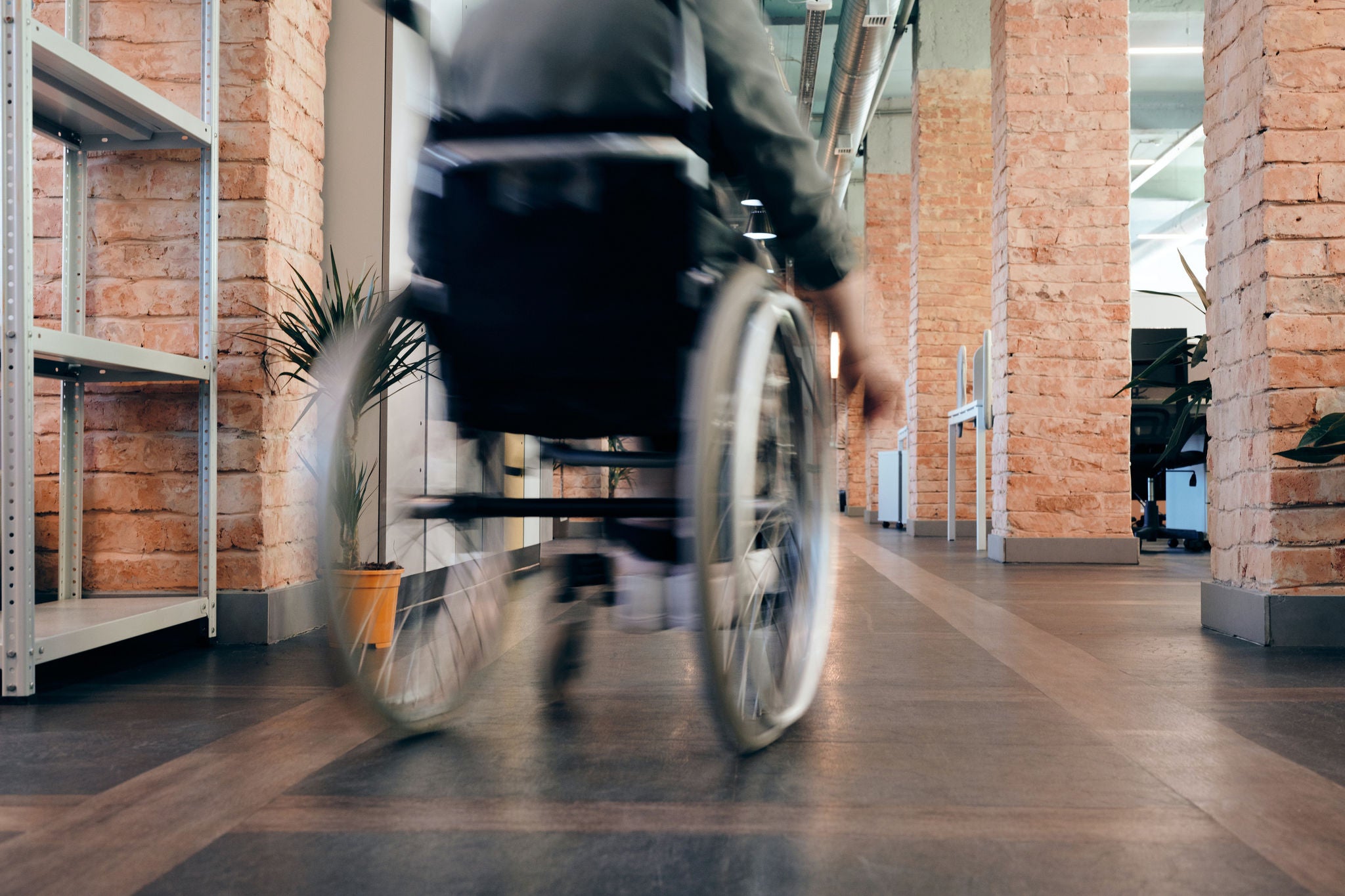 Persona en silla de ruedas desplazándose por el pasillo de una oficina, en una imagen con efecto de movimiento que transmite accesibilidad y dinamismo.