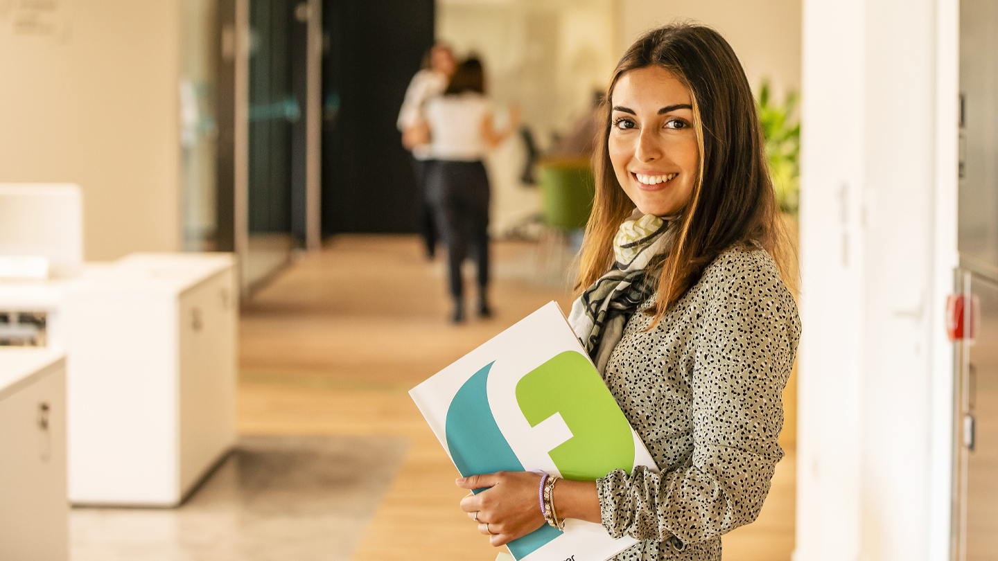 Smiling employee holding a corporate folder with the Ferrer Group logo in the company's offices.