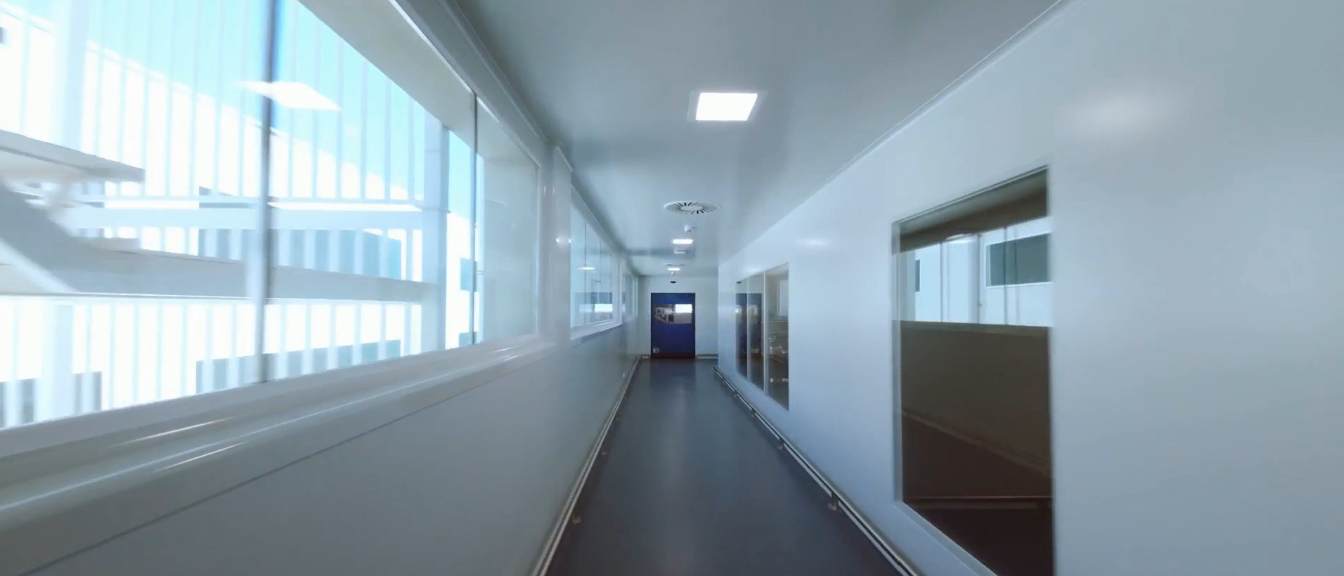 Passadís interior de les instal·lacions de Ferrer, amb parets blanques, finestrals i portes d'accés a diferents àrees de treball