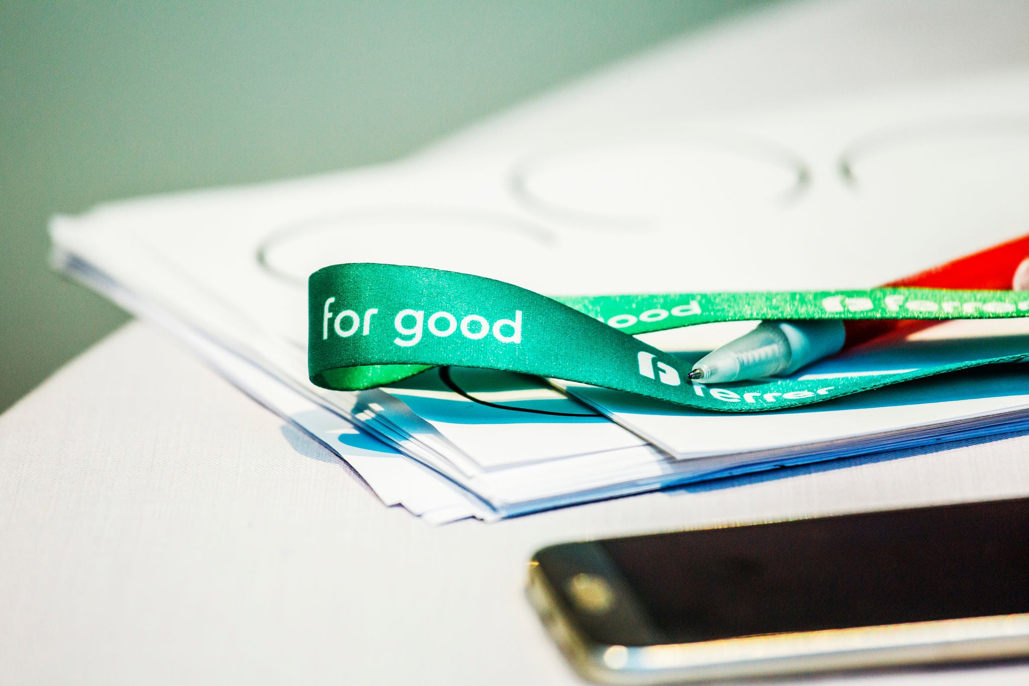 Detail of a work table with documents, a mobile phone and a green Ferrer ribbon with the message "Ferrer for good".