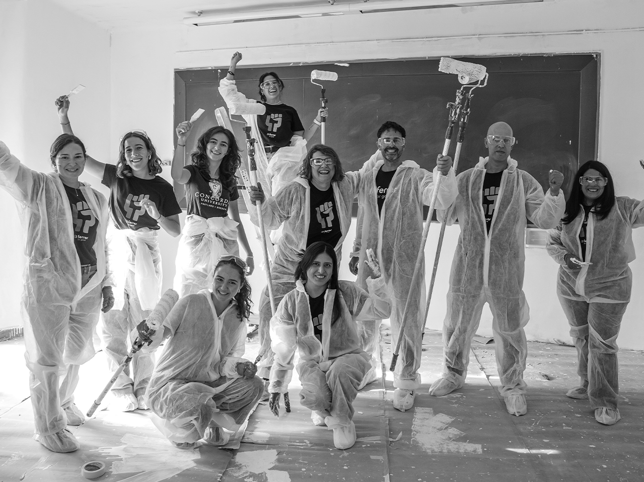 Group of volunteers in a collective action initiative, equipped with protective coveralls and rollers to paint a school classroom with Grupo Ferrer.