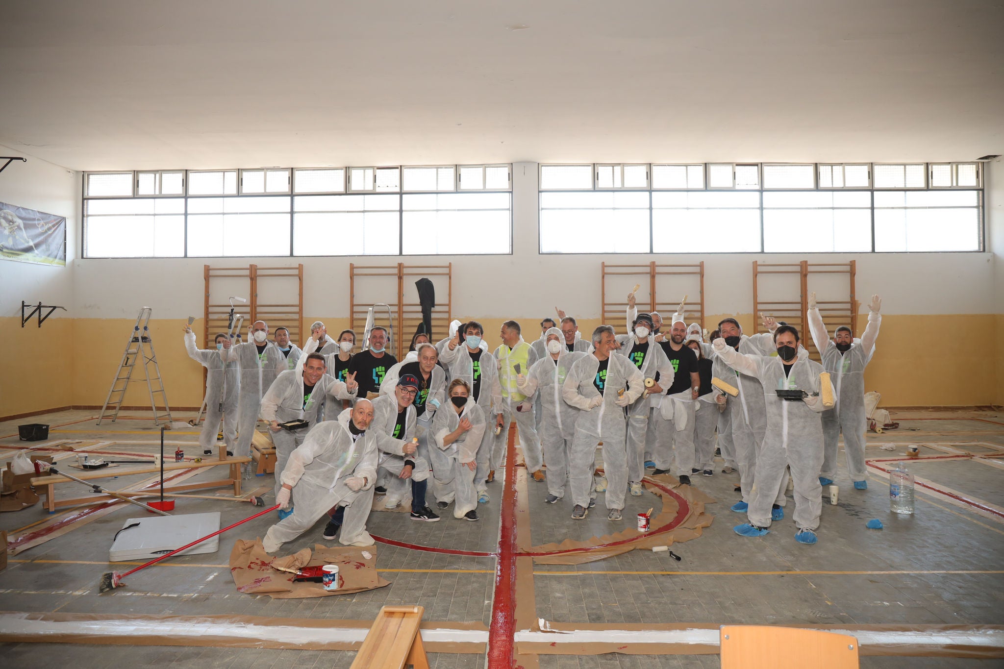 Grup de persones amb vestits de protecció blancs posant en un gimnàs en obres amb materials de pintura.